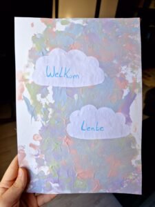 een baby die verft met pastel kleuren en ene lente tekening maakt met wolkjes