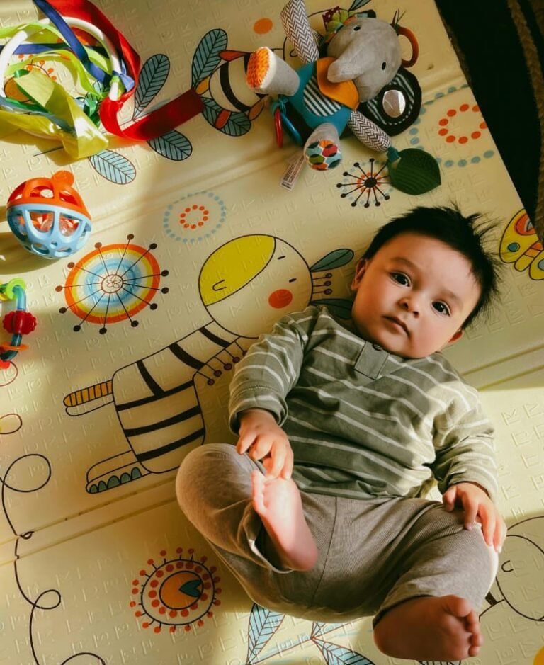 baby ligt op een speelkleed met speelgoed er om heen
